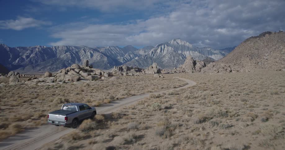 Grey pickup truck driving through a road surrounded by rocky mountains outdoors during day time