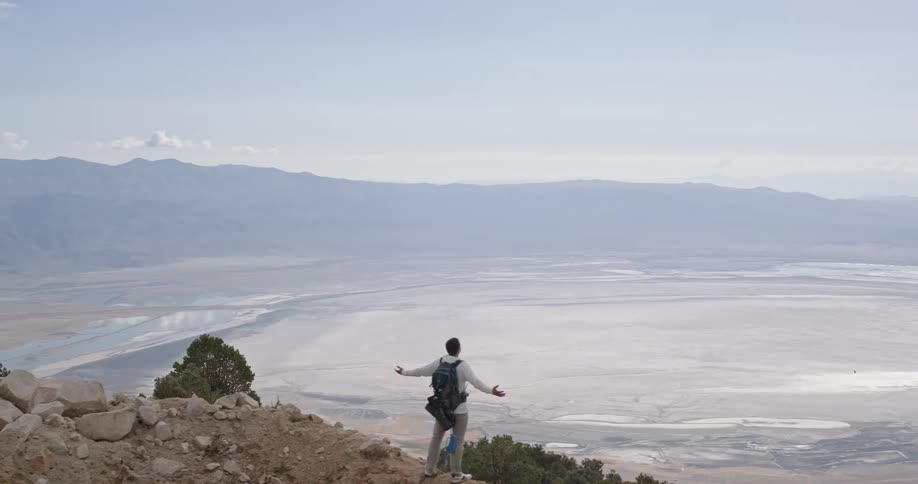 Aerial of a young man standing outdoors on a rocky mountain summit during daytime