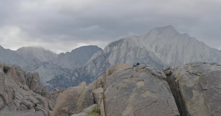 The man is climbing over the tall boulders by the mountain range