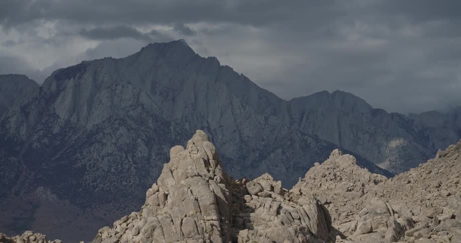 A dark mountain range in the background framed by lighter jagged rock formations in the immediate foreground all beneath an overcast sky with heavy cloud cover