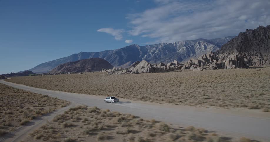 Car driving on dirt road in desert landscape with rock formations and clear sky
