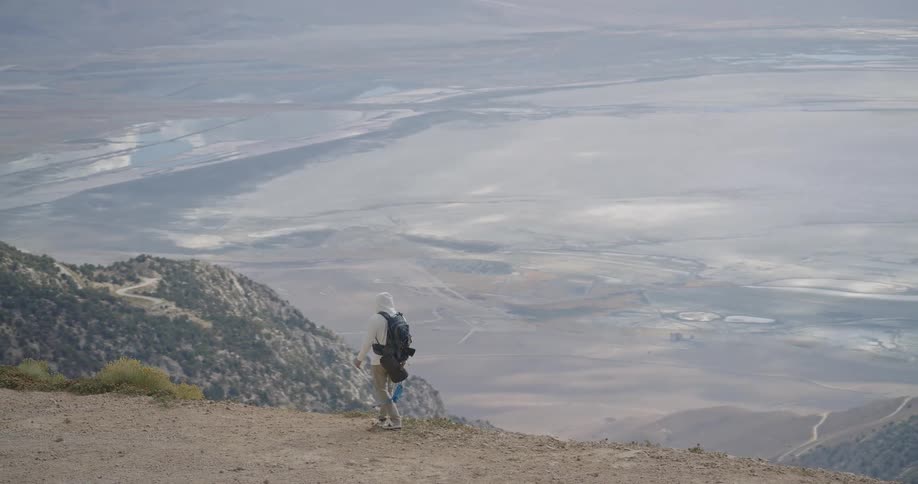 Person standing on dirt trail overlooking salt flat surrounded by mountains