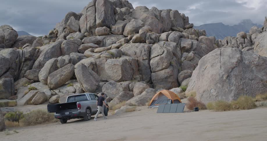 Person picks up equipment from suv at mountain campsite with tent and rock formations around