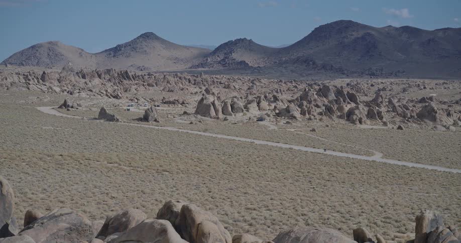 A sprawling area of small spired rock formations and flat brushcovered desert crossed by an unpaved road with large bare hills and mountains forming the horizon