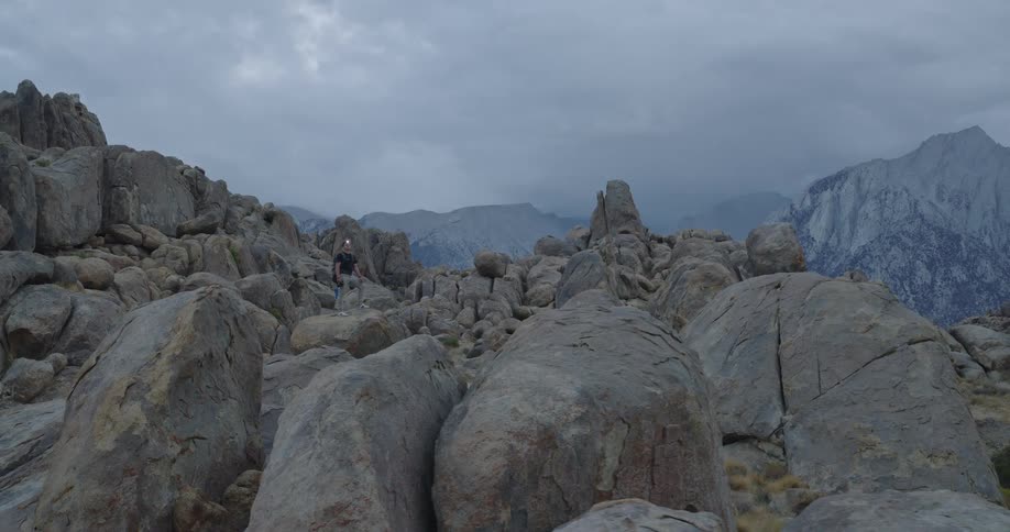 Man among rocks in mountainous terrain with clouds covering part of the mountains in the background