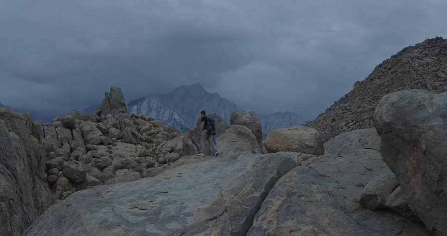 Male hiker walks across a rock formation in a boulder field located near a hill on an overcast day