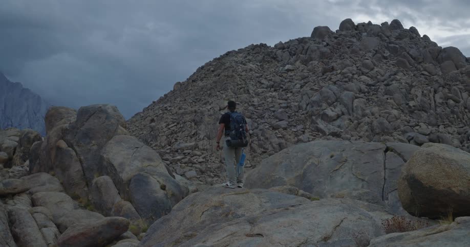 Person walking among rocks on a mountain trail under a cloudy sky