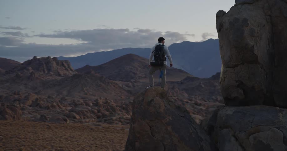 Man standing on rock formation overlooking salt flat at sunset