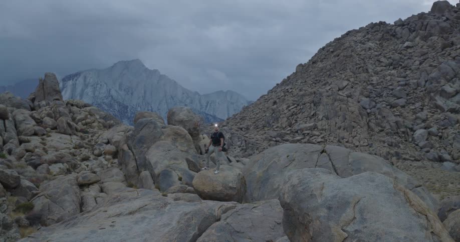 Person walks among rocks under a cloudy sky with a mountain in the background