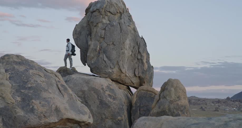 The man is overlooking the mountains from the top of a pile of boulders