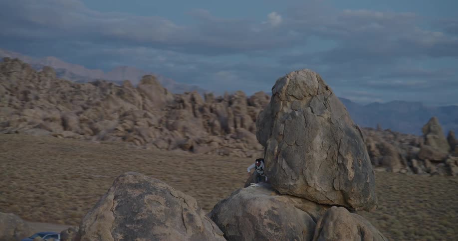 Male hiker climbs a rock formation located near the mountains after the sun has sunk behind the mountains