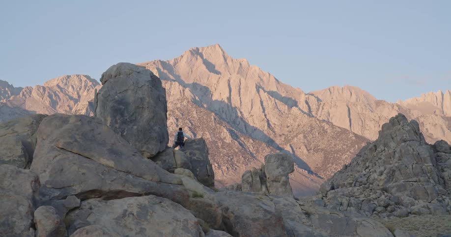Steep mountains with rock formations in the foreground and two people standing on one of them