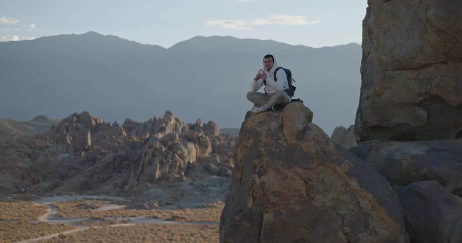 The man sits with his legs folded on a large boulder