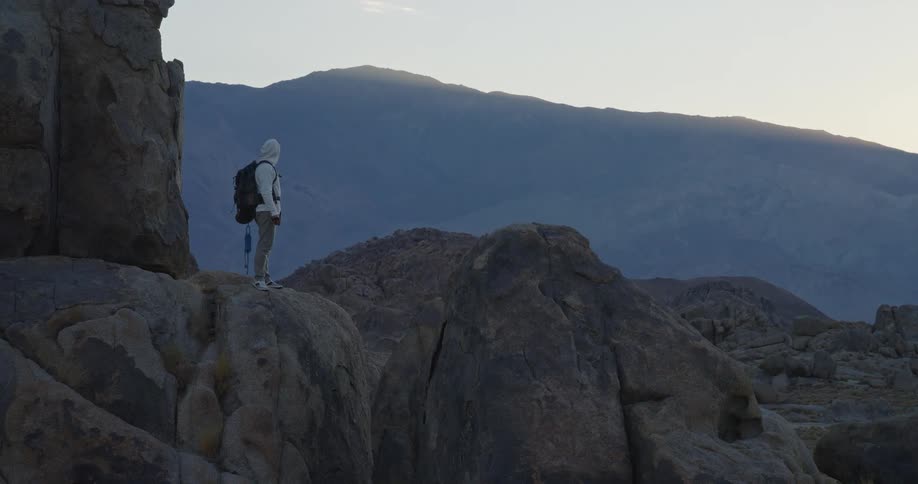 Person in white outfit gazes at horizon on rocky terrain at dusk