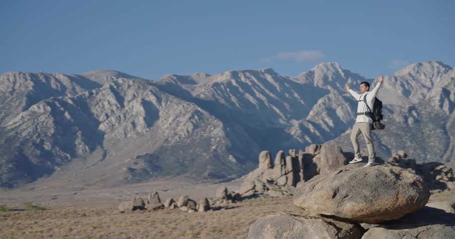 Man raises arms atop rocky formation in mountainous landscape