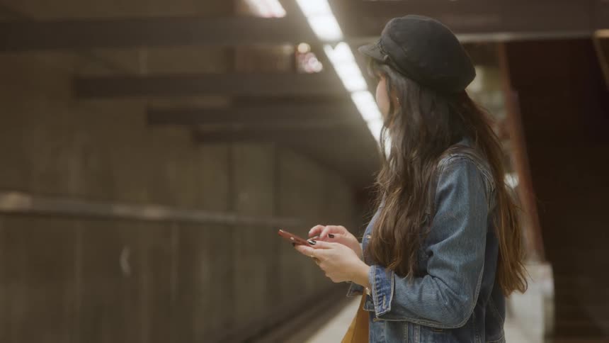 A young woman waits for a train at a terminal while using her phone