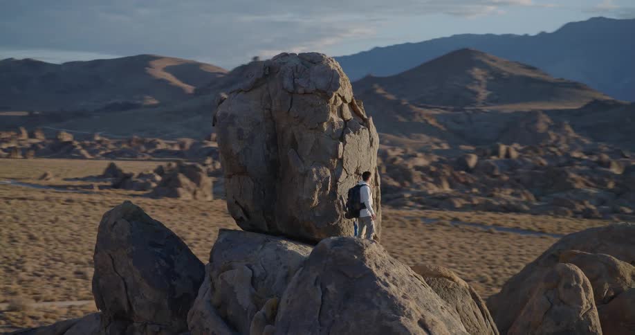 Man standing on rock beside rocky formation in desert region with mountains in the background