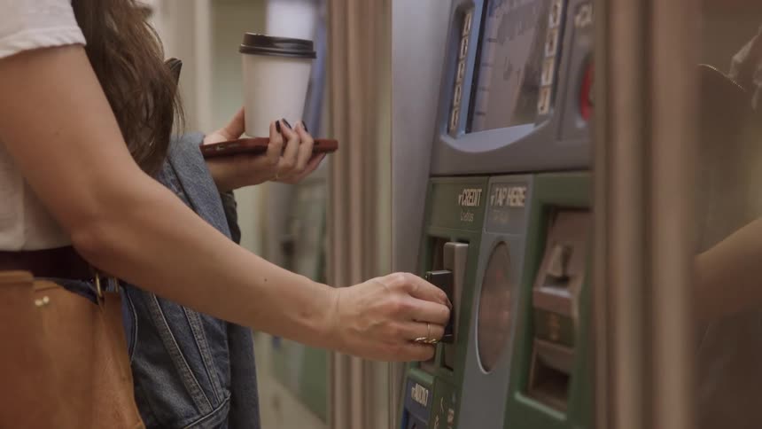 Close up of a young woman inserting and withdrawing her card from a payment machine during daytime