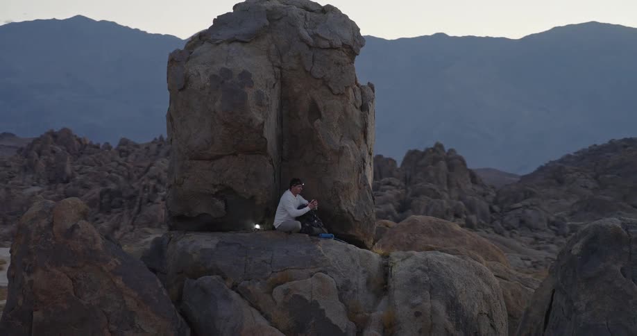 The man moves around on top of the huge boulders