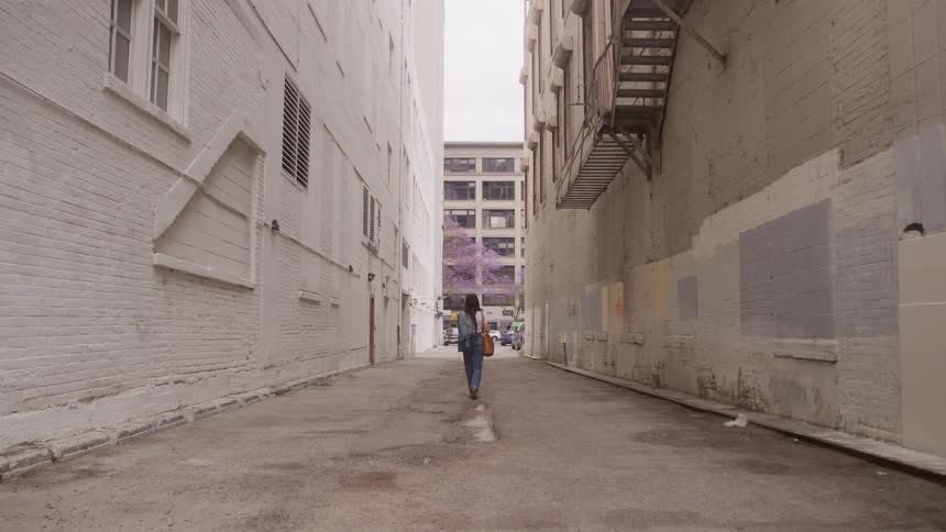 Woman walking through urban alleyway between tall buildings with backpack on