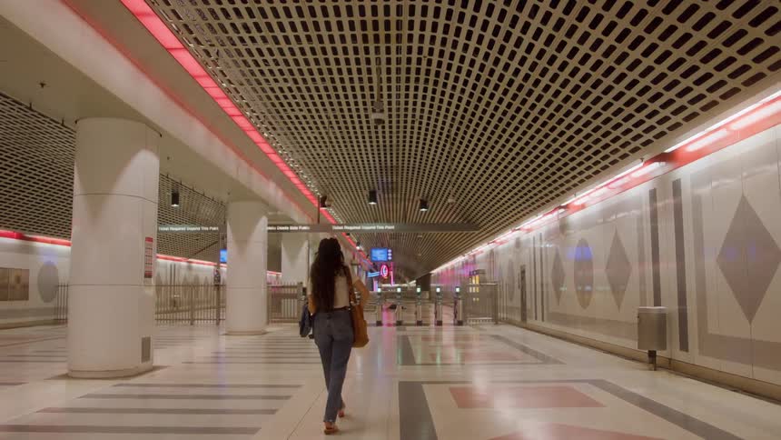 Woman carrying a handbag walking indoors towards a row of turnstiles in a station