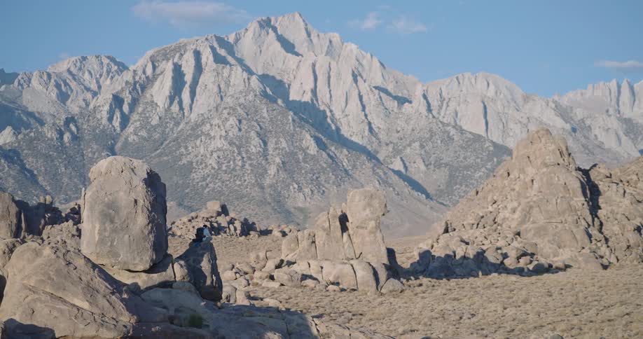 A male hiker rests among tan boulders in bright morning light with towering pale granite peaks behind looking calm