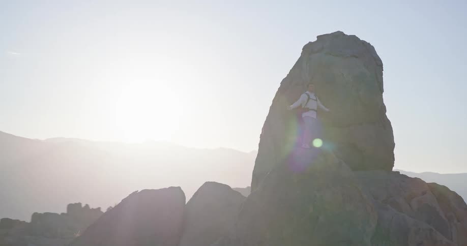 Man carrying a backpack standing on top of a tall rock in a wilderness landscape with his arms outstretched outdoors during day time