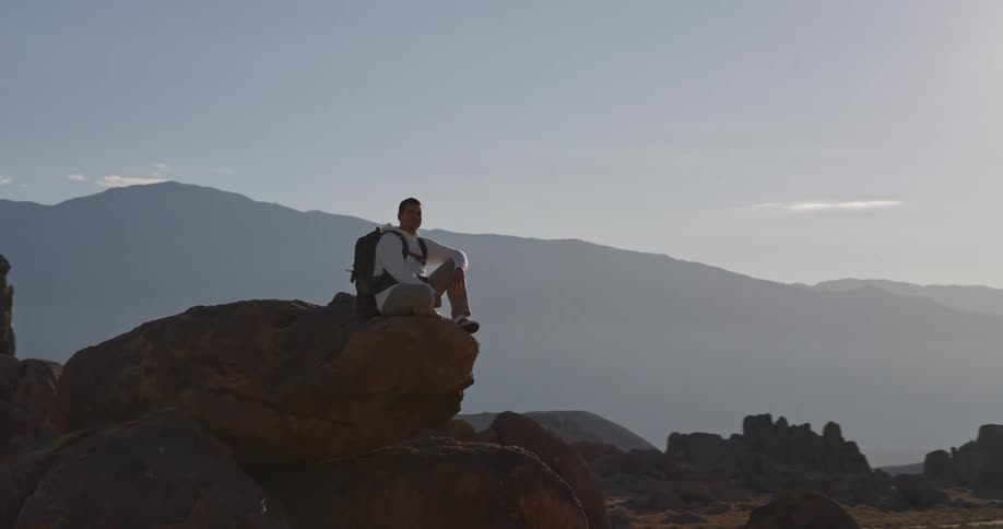 The man sits on the edge of the stack of tall boulders