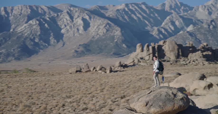 Hiker stands on a rock overlooking rocky terrain and distant mountains
