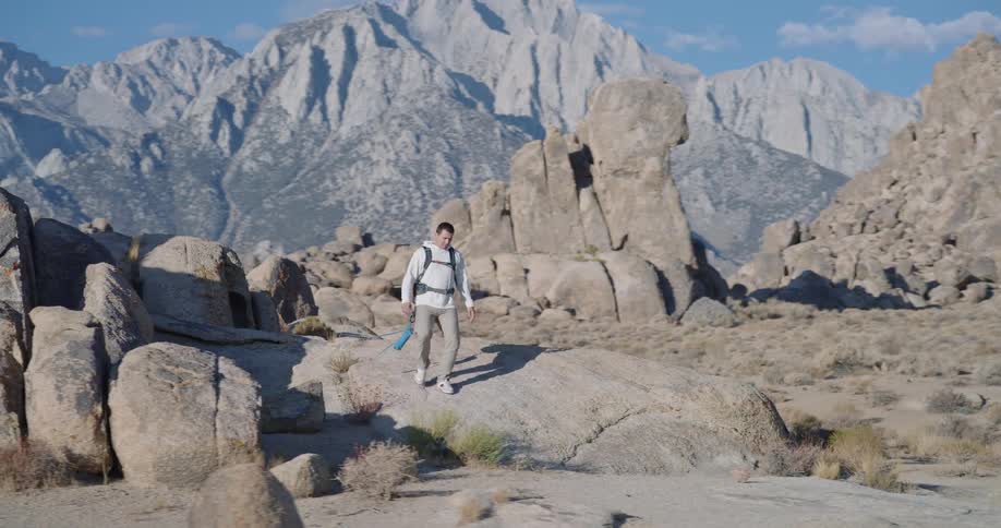 Man walks among rocks under the sun with mountains in the background