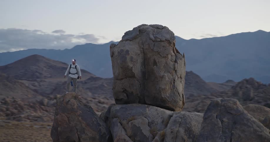 Man standing on rock formation in mountainous and arid area under cloudy sky