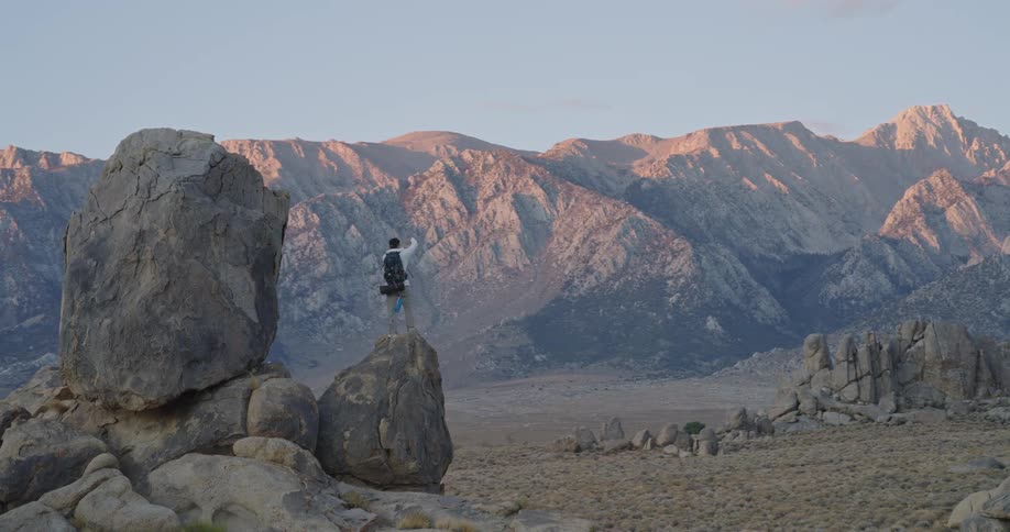 The man perched on the mountain reaches his arms out