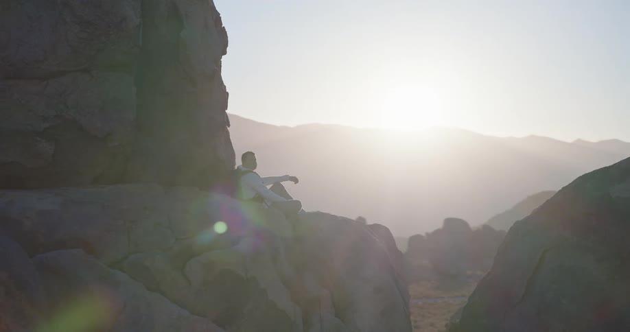 Man sitting among rocks looks at the horizon at sunset
