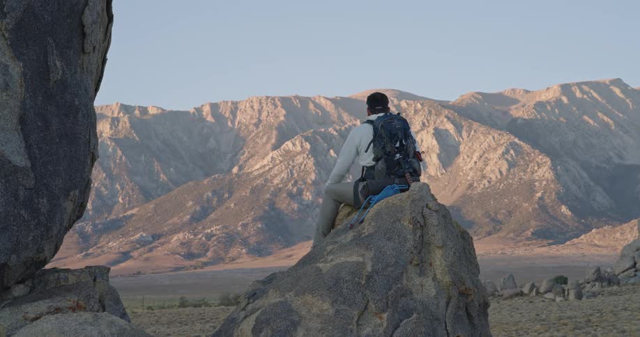 A hiker sits on a large boulder in a deep rocky canyon