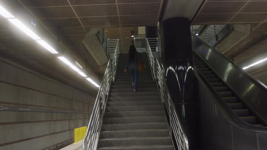 The woman is walking up the stairwell in the subway