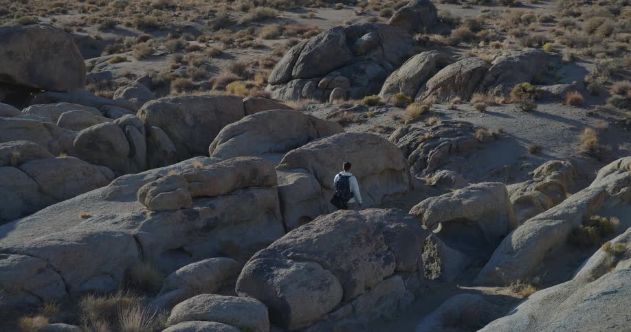 A man carrying a backpack hikes through rocky rough terrain in the wilderness at midday