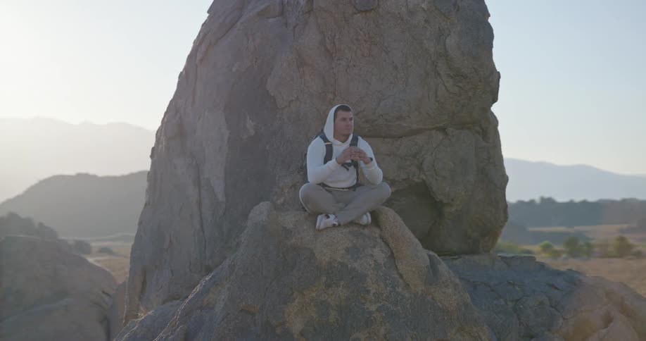 Man sitting on a rock looking around the landscape in a mountainous area outdoors during day time