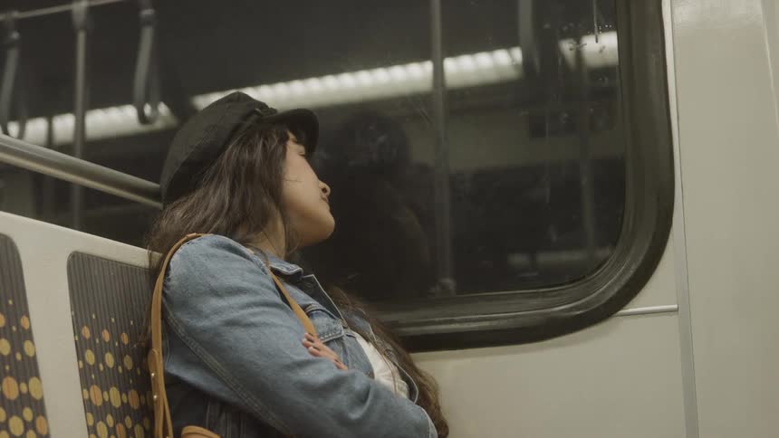 A young woman wearing a black cap and a jean jacket sleeps peacefully while riding the train