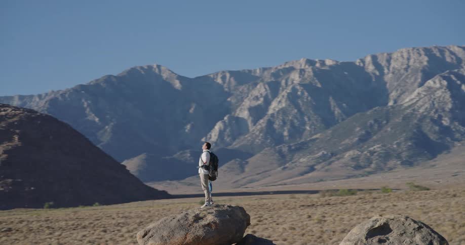 Man standing on rock opening his arms and observing mountain range in arid region