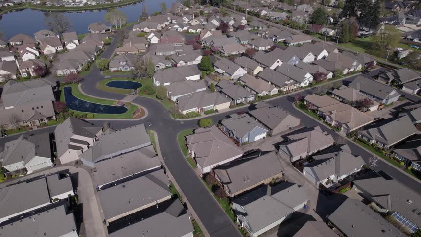 A residential neighborhood overlooks a serene lake at midday with sunlight glinting off the water and houses nestled among trees lining the shore