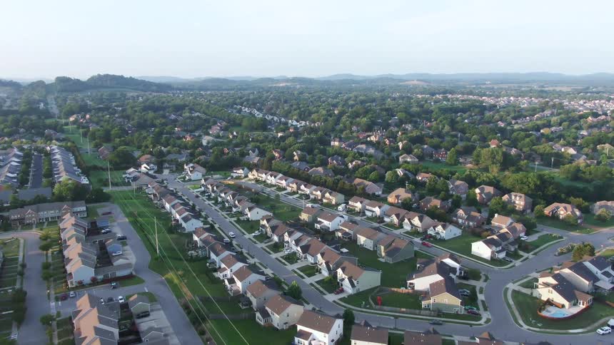 Aerial view of suburban neighborhood with curving streets singlefamily homes and wooded area in the background