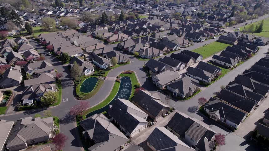 The video is a highangle aerial shot showing a densely populated residential suburb with rows of housesa central beautifully manicured green space with two small pondlike water features provides a visual break from the surrounding build