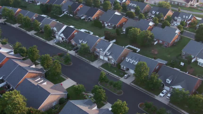An aerial view captures a quiet suburban neighborhood with neat rows of houses green lawns and trees