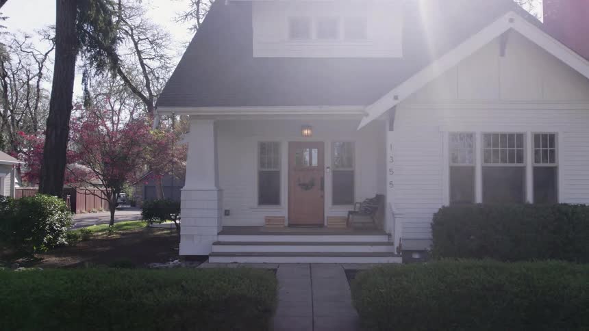 White house with pitched roof and blooming garden lit by sunlight
