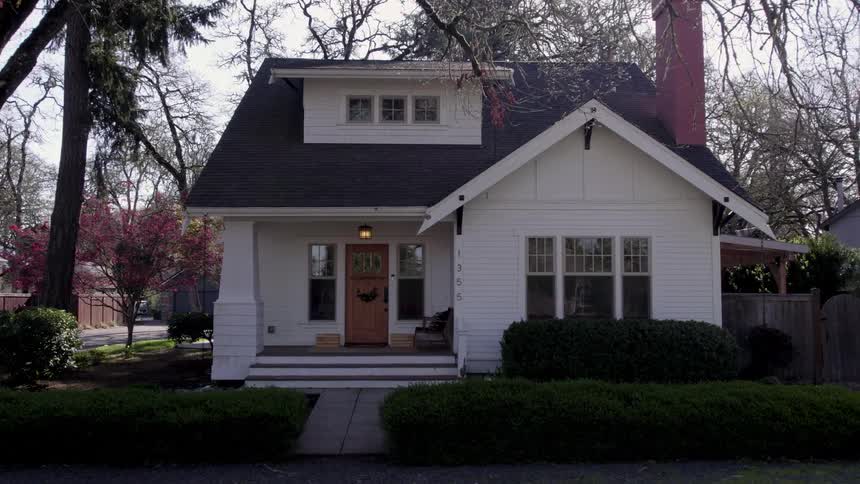 White house with porch surrounded by bushes and trees under clear sky
