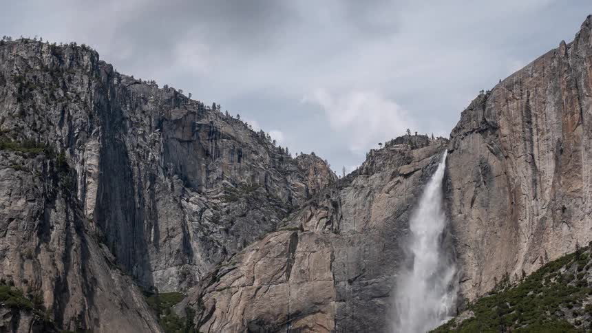 Tall waterfall descends along rocky cliff surrounded by sparse vegetation