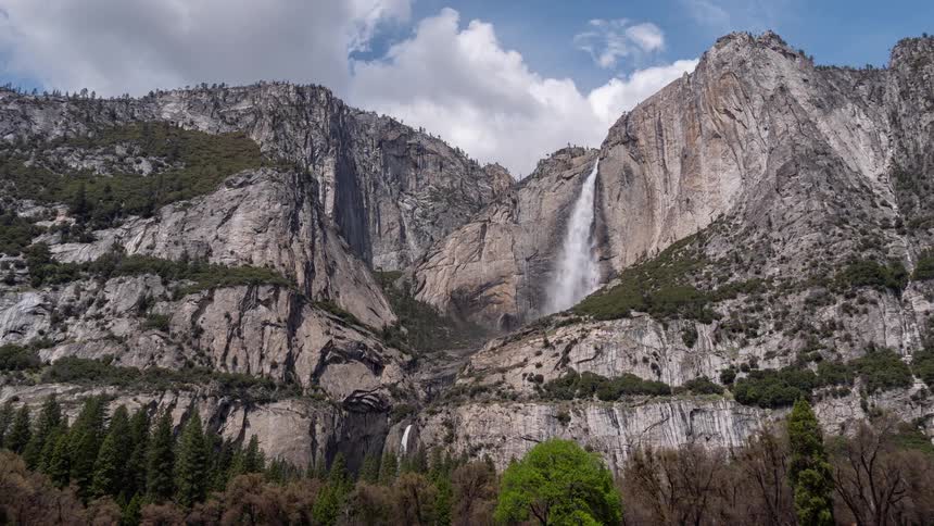 Yosemite falls descends along granite cliffs surrounded by vegetation