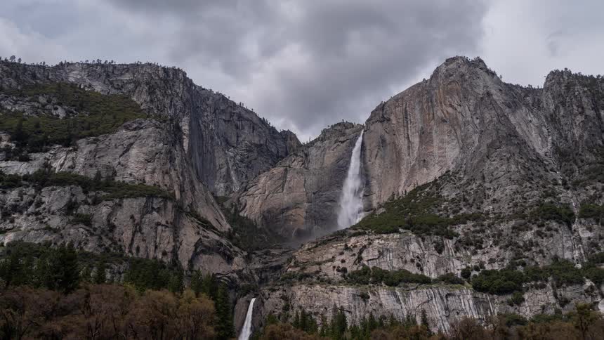 Waterfall split into two sections descends along rocky cliff surrounded by forest