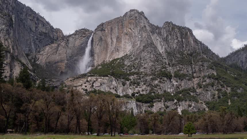 A mountain with a waterfall and a freeway running alongside it surrounded by lush green vegetation at midday