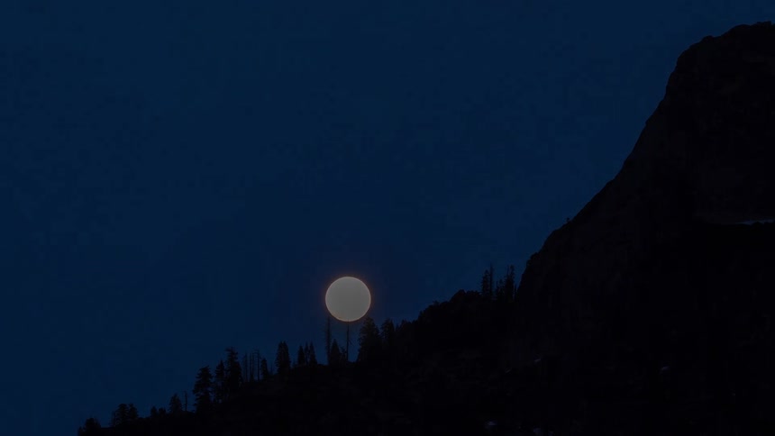 Full moon lighting forested mountain ridge under deep night sky